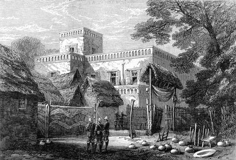 Drawing. A black and white illustration of a grand villa situated within a rustic, rural setting. The clean geometry of the stone building contrasts with its surrounding buildings and structures made from wood and straw. Two separate group of smartly-dressed soldiers or guards stand in the surrounding area, wearing belted coats, knee high boots and helmets.